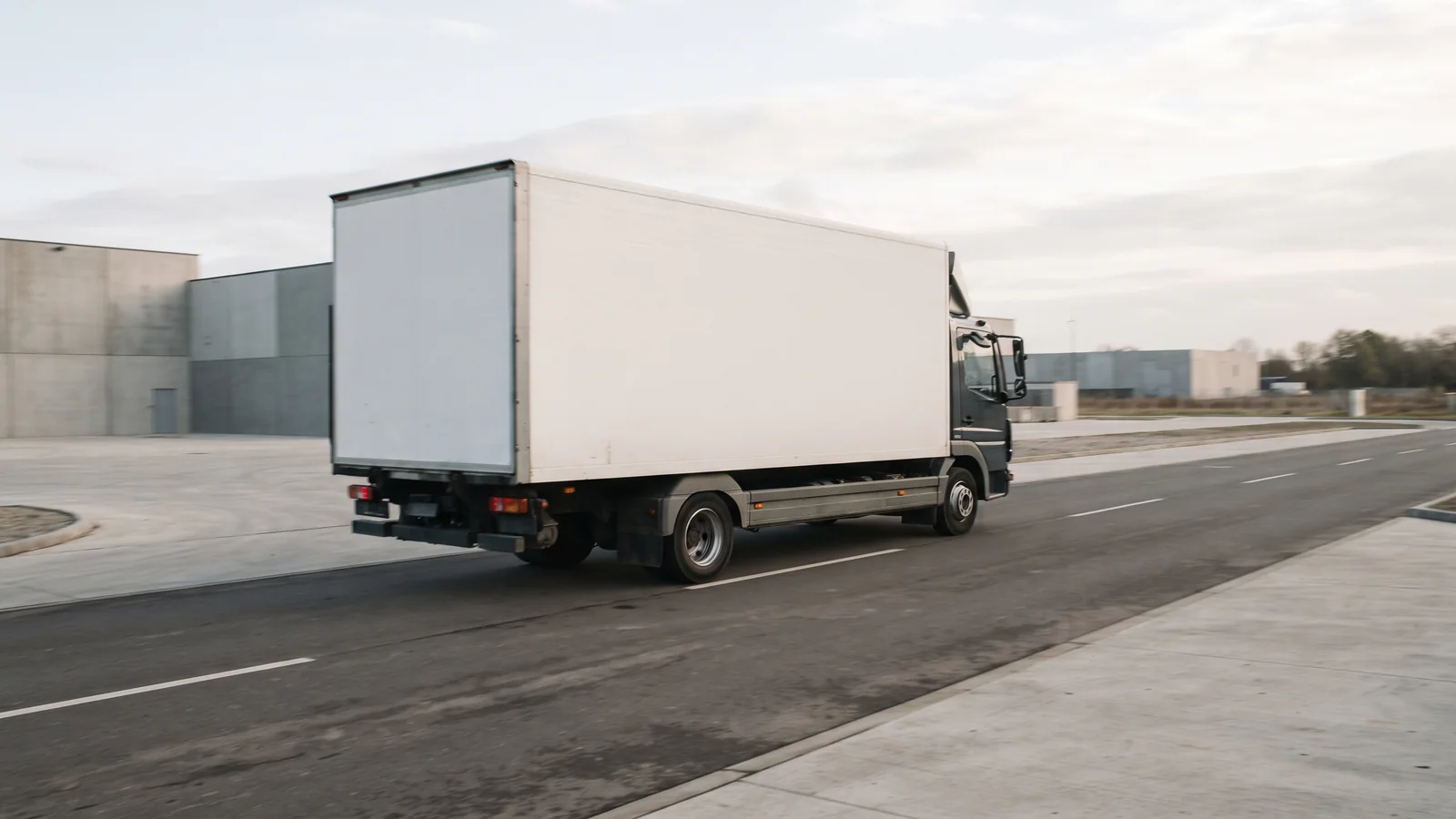 KI-generiertes Symbolbild: Ein neutraler, unbeschrifteter Güter-Lkw fährt durch ein Gewerbegebiet.